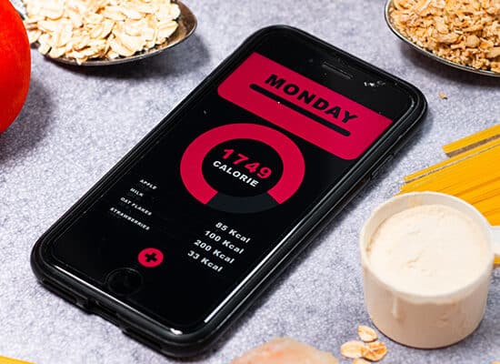 telefon pe masa cu aplicatie de numarat calorii inconjurat de alimente