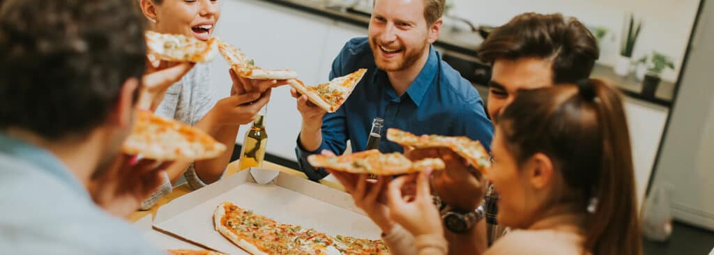 Grup de oameni mananca pizza si zambesc pofte alimentare