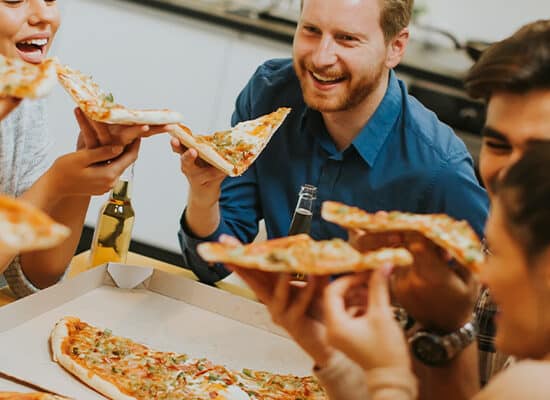 Grup de oameni mananca pizza si zambesc pofte alimentare