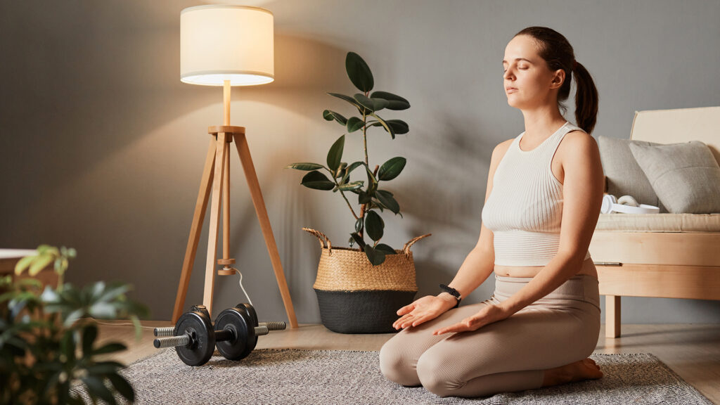 Femeie in pozitie de yoga, meditateaza in sufragerie 