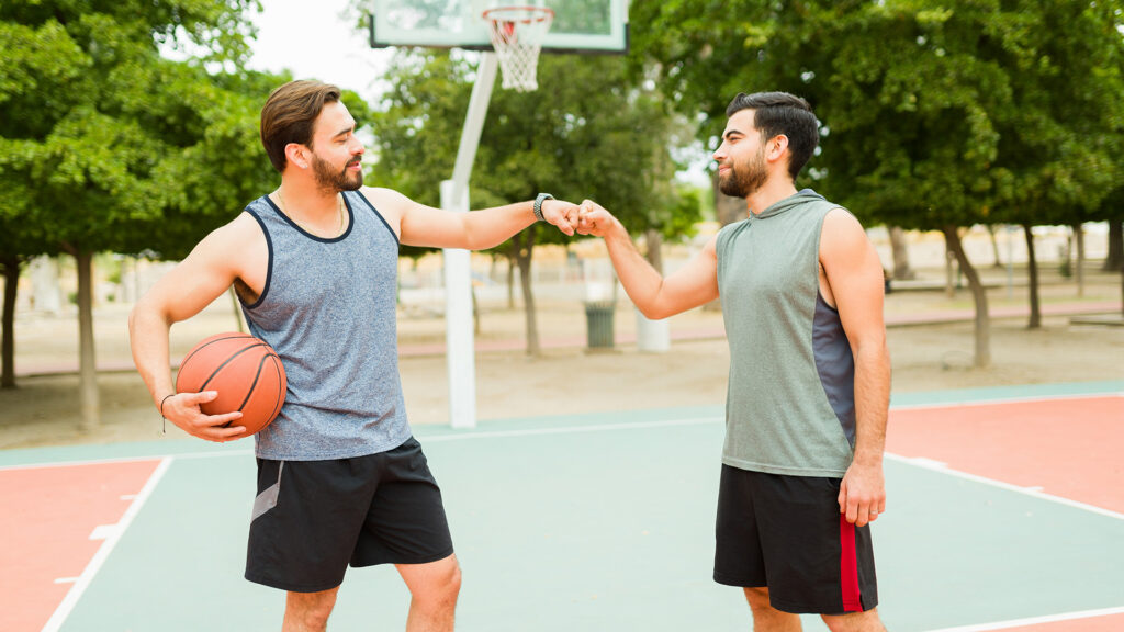 Prieteni joaca basket pe teren in aer liber