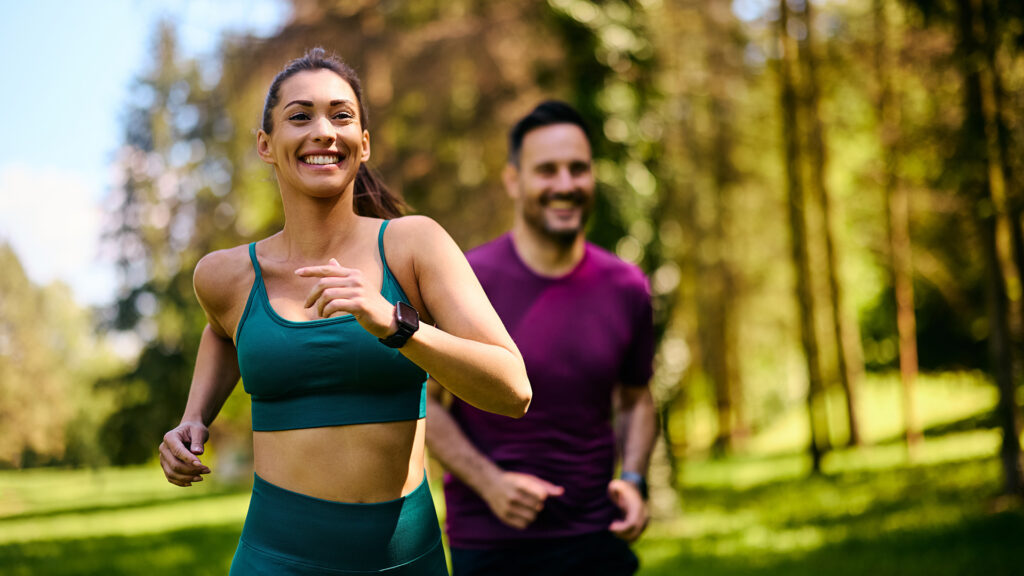 o femeie si un barbat practica sport, alearga in natura, fericiti 