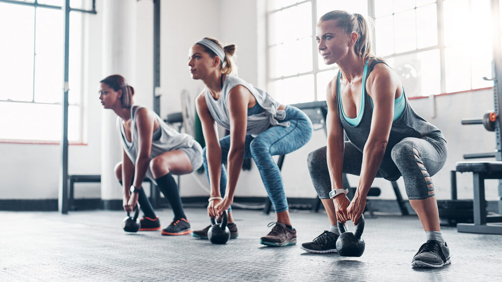 Trei femeie in sala de fitness ridica greutati in pozitie de fandare