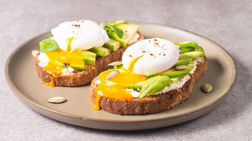 2 felii de toast cu crema de branza,  avocado si oua posate pe farfurie