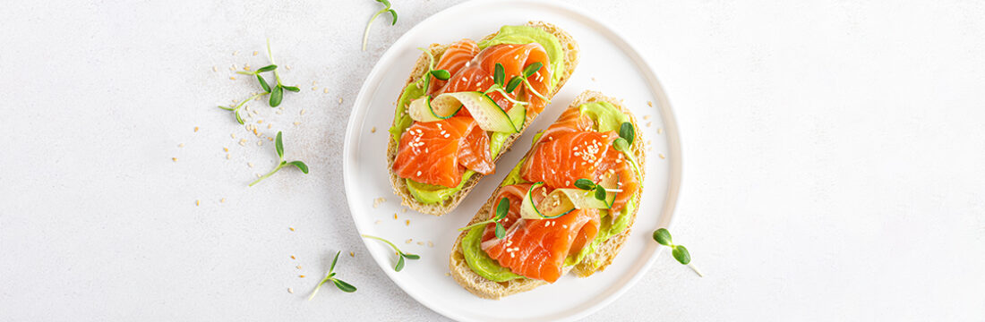 Doua felii de toast cu somon si avocado pe farfurie alba pe masa