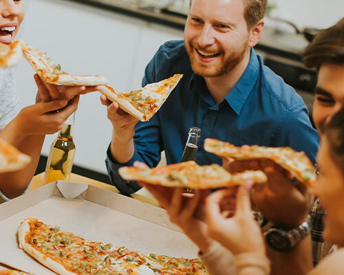 Grup de oameni mananca pizza si zambesc