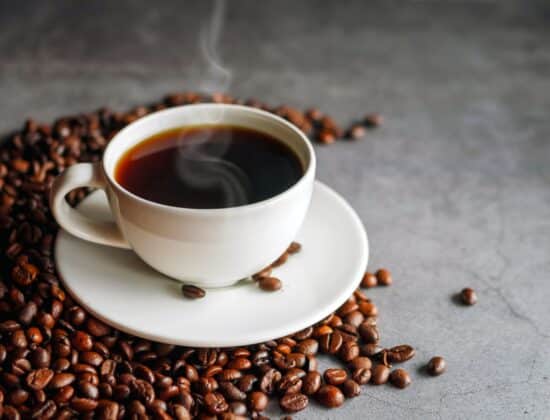 cafea fierbinte in ceasca alba, iese abur din ea, boabe de cafea in jur