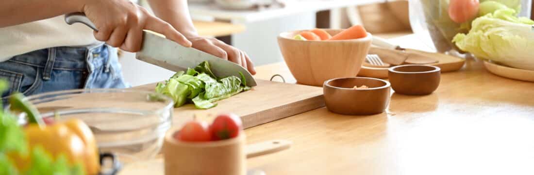 Imagine de aproape, mâinile unei femei care taie salată verde pe un tocător de lemn