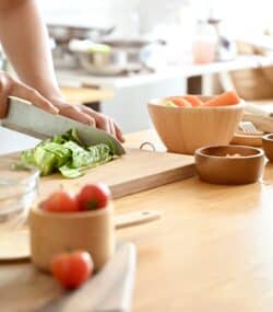 Imagine de aproape, mâinile unei femei care taie salată verde pe un tocător de lemn