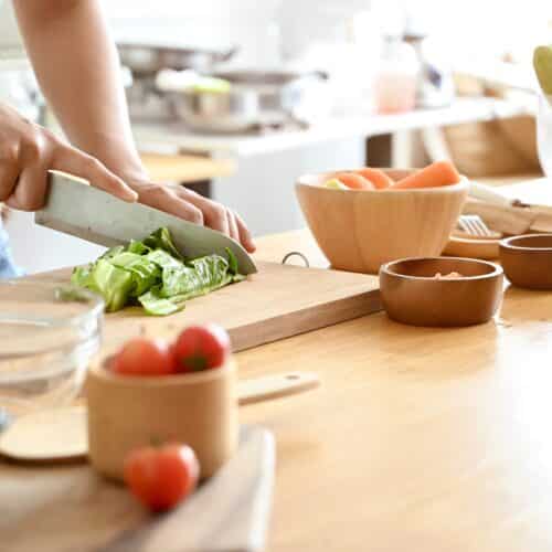 Imagine de aproape, mâinile unei femei care taie salată verde pe un tocător de lemn