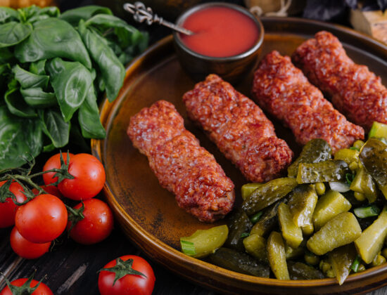 Imagine cu mici în farfurie, înconjurați de salată de murături, roșii, spanac, sos de roșii.