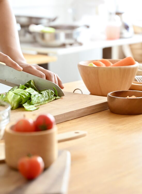 o femeie toaca alimente pe un tocator, pregateste mancare sanatoasa, legume, in bucatarie