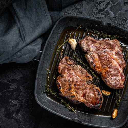 Carne de porc pe tigaie, pe fundal negru