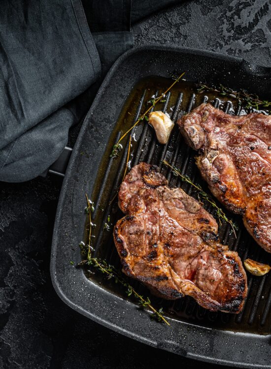 Carne de porc pe tigaie, pe fundal negru