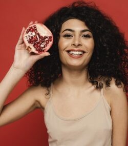 femeie zambitoare cu o rodie valori nutritionale in mana pe fundal rosu