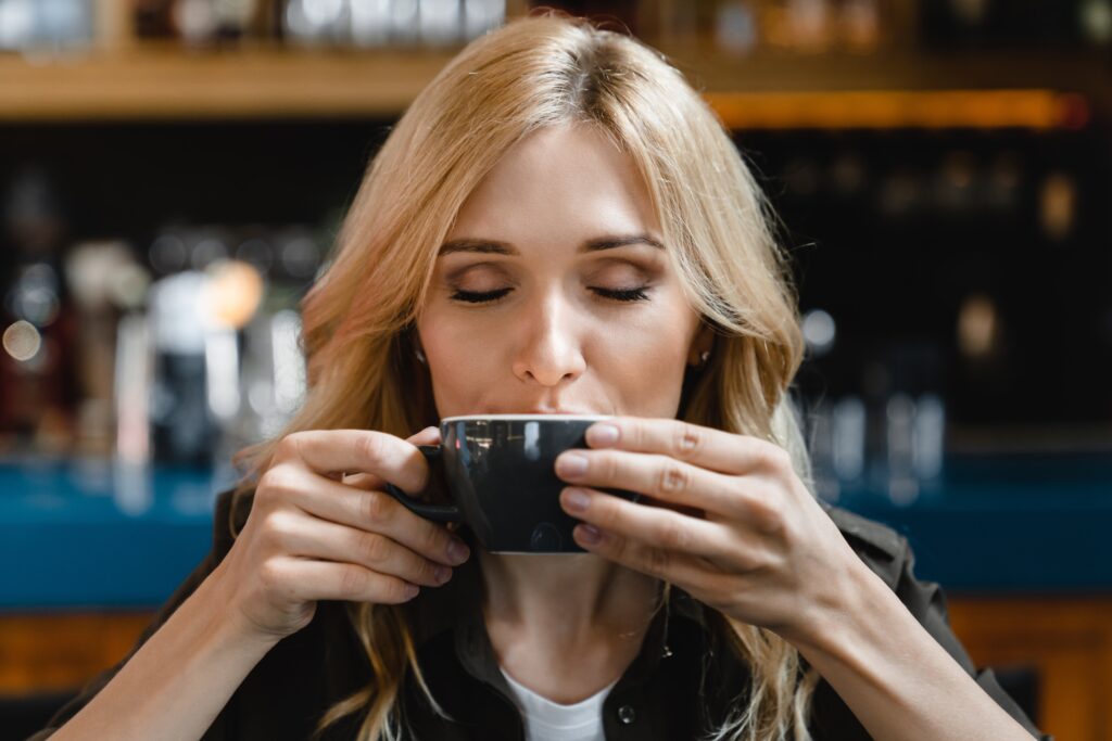 o femeie savureaza o cafea in ceasca, sta cu ochii inchisi