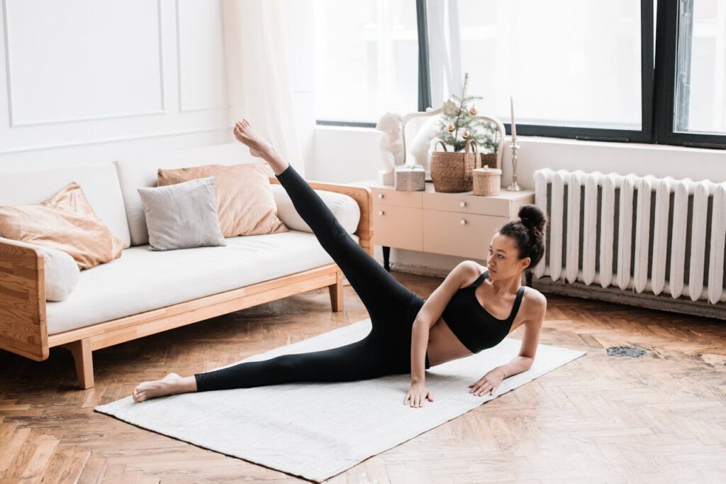 o tanara face exercitii la saltea, acasa, in sufragerie, exercitii fizice pentru picioare si abdomen