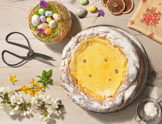 Imagine de sus cu o pască așezată pe masă, înconjurată de flori și ouă de paște