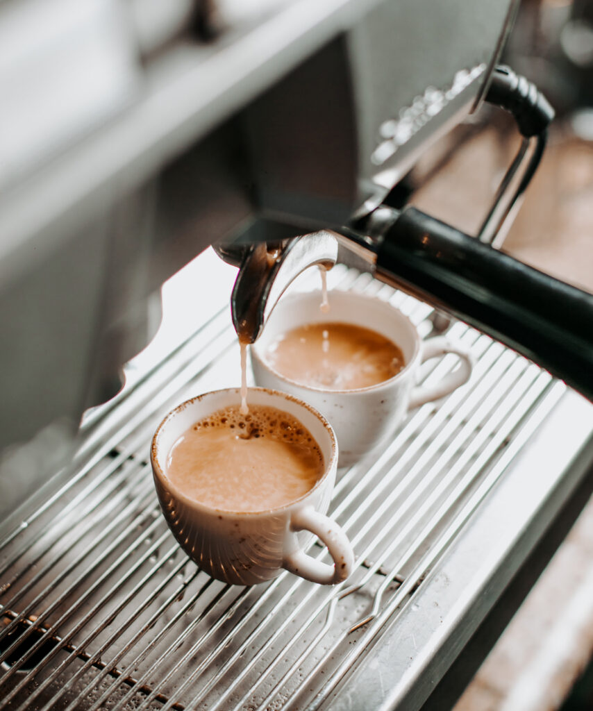 doua cesti umplute cu cafea de un espressor