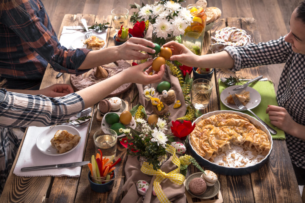 Familie care sparge ouă de Paște colorate cu vopsea de ouă naturală în jurul mesei festive