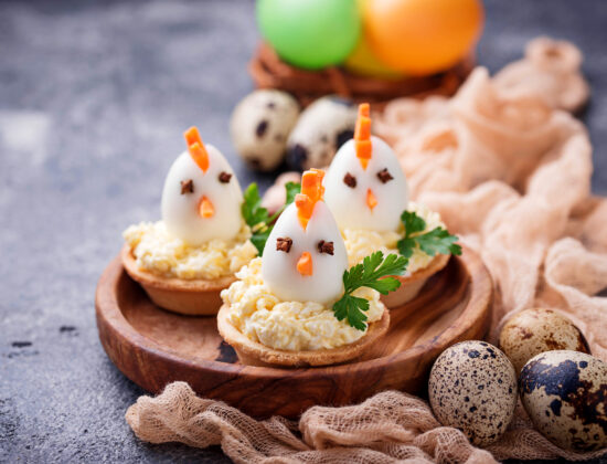 Imagine de aproape cu aperitive de paste cu aspect de puișori făcute din jumătăți de ouă și bucăți de morcov, așezate pe un blat tare rotund