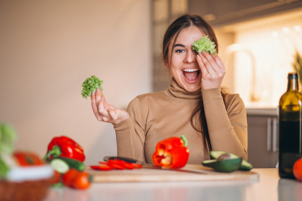 Imagine din față cu o femeie fericită care taie legume proaspete și zâmbește către cameră