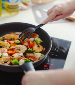 Imagine de aproape cu omainile unei persoane care prepara creveti sote la tigaie, sursa sanatoasa de proteina pentru dietele de slabit cu proteine