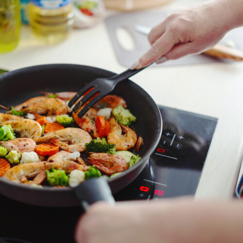 Imagine de aproape cu omainile unei persoane care prepara creveti sote la tigaie, sursa sanatoasa de proteina pentru dietele de slabit cu proteine