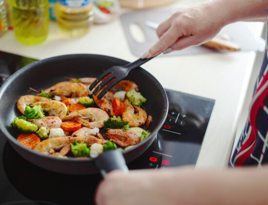 Imagine de aproape cu mainile unei persoane care prepara creveti sote la tigaie, sursa sanatoasa de proteina pentru dietele de slabit cu proteine