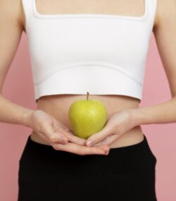 Imagine din față cu talia unei fete tinere care ține un măr în dreptul abdomenului, simbolizand un microbiom intestinal sanatos