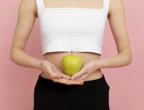 Imagine din față cu talia unei fete tinere care ține un măr în dreptul abdomenului, simbolizand un microbiom intestinal sanatos