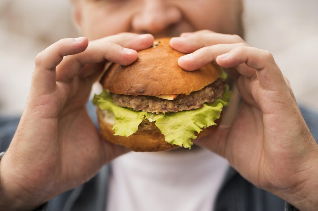 Imagine de aproape cu un barbat tanar care mananca un burger