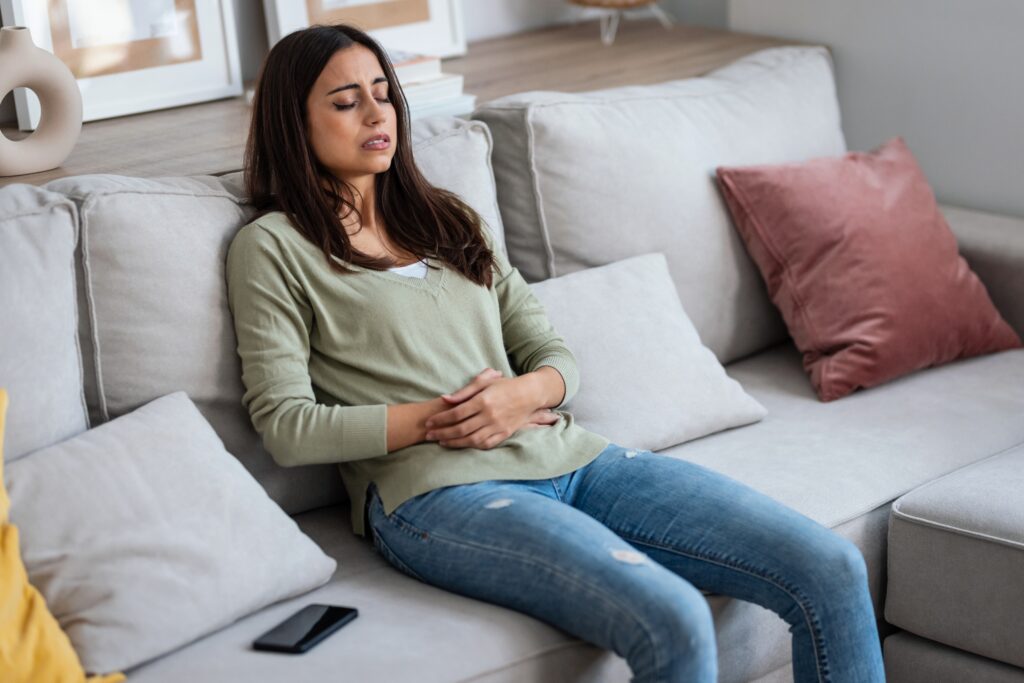 tanara care se simte rau, cu mainile pe abdomen, sta pe canapea