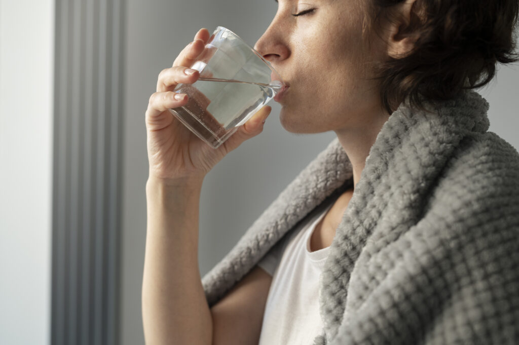 Femeie tanara bea un pahar de apa pentru a preveni deshidratarea la raceala