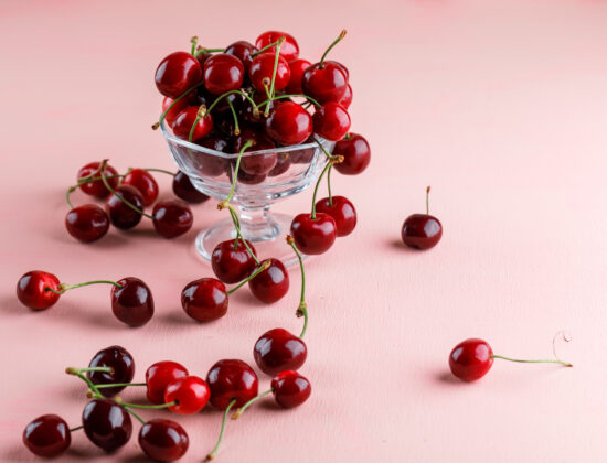 Cireșe într-o sticlî transparentă cu picior, pe un fundal roz