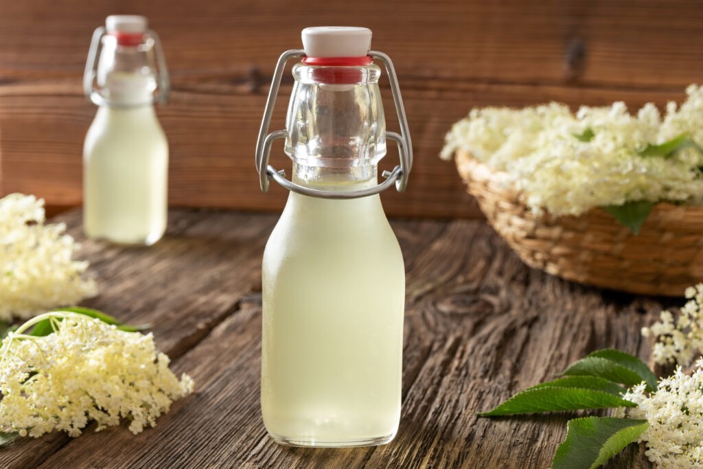 sirop de soc intr-o sticla, pe masa, cu flori de soc in jur