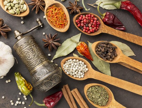 Imagine de sus cu o rasnita si diferite tipuri de condimente pentru slabit in linguri de lemn, pe un fundal negru