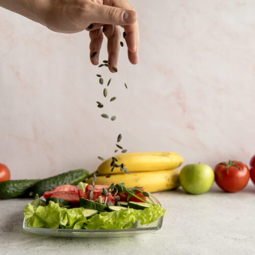Imagine de aproape, mâna unei persoae care presară seminte peste un preparat cu alimente naturale din dieta fulger