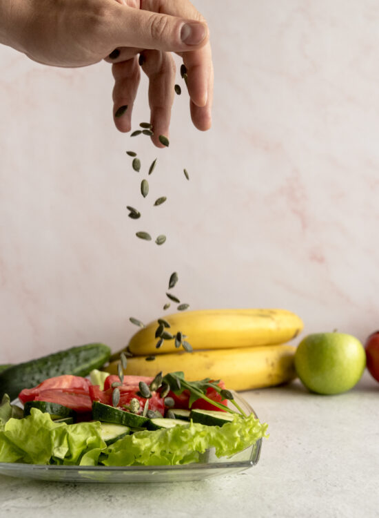 Imagine de aproape, mâna unei persoae care presară seminte peste un preparat cu alimente naturale din dieta fulger