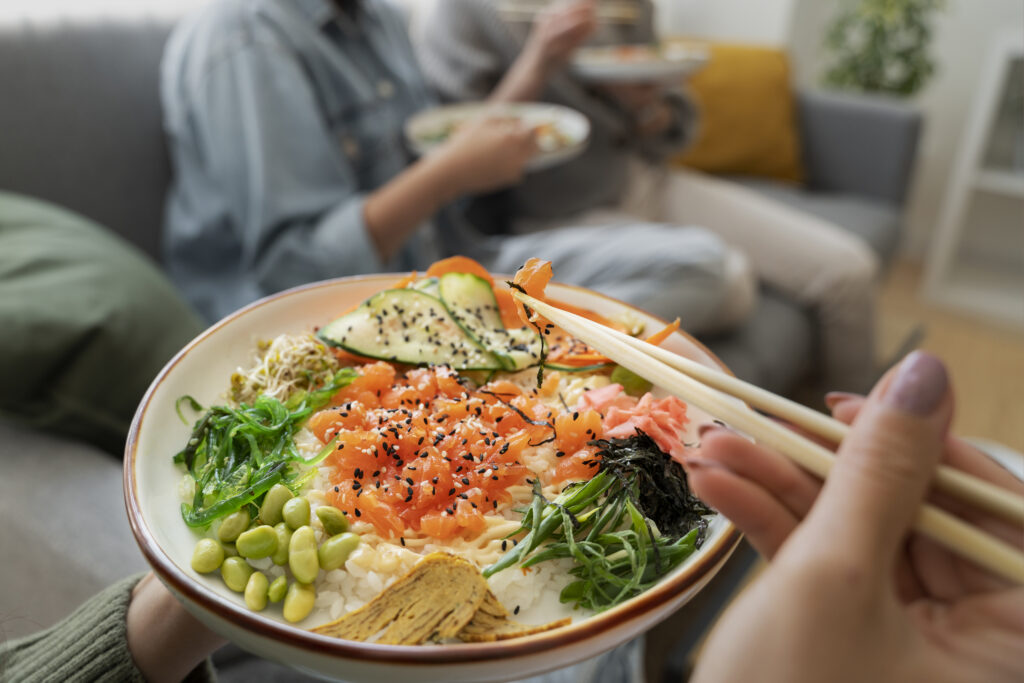 Femeie care mănâncă un bol cu orez, legume și pește, preparat specific în dieta japoneză