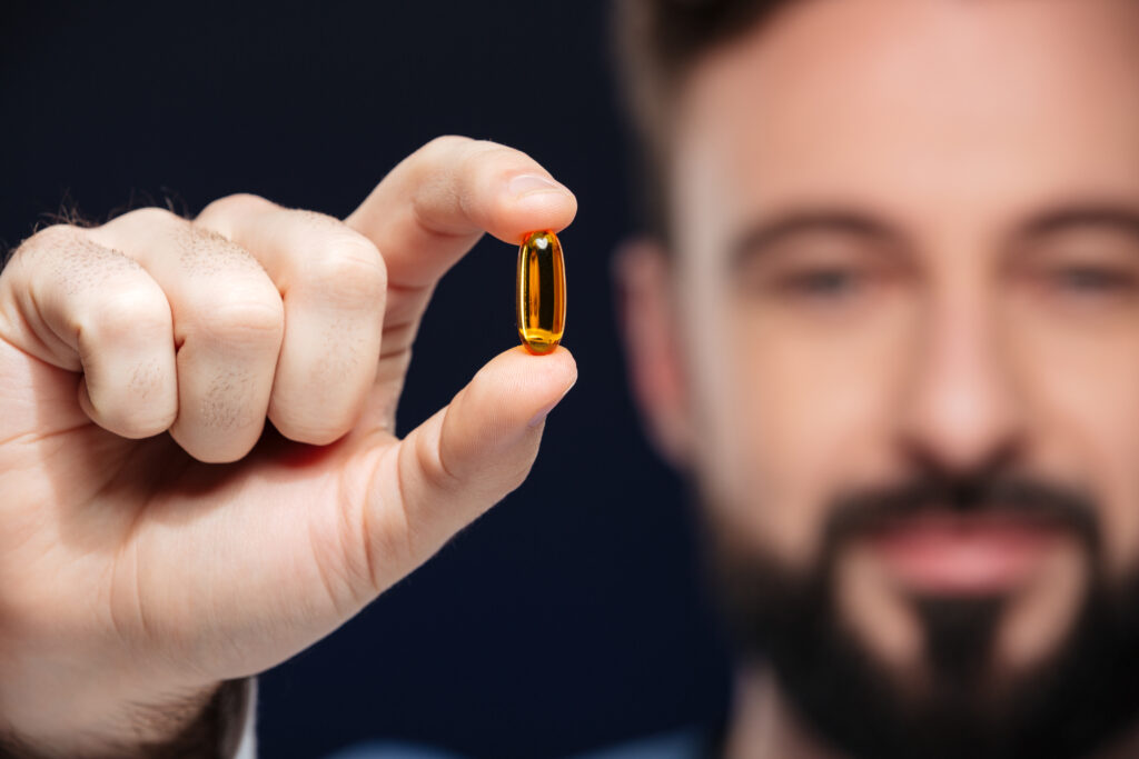Barbat arata catre camera o pastila de omega 3, supliment alimentar optim in dieta japoneza