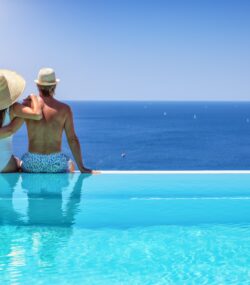 cuplu se imbratiseaza la marginea unei piscine infinite si se bucura de privelistea spre mare