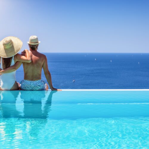 cuplu se imbratiseaza la marginea unei piscine infinite si se bucura de privelistea spre mare