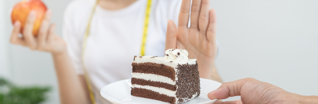 Femeie refuzând o felie de tort și preferând să mănânce un măr, pentru a-și reduce pofta de mâncare.