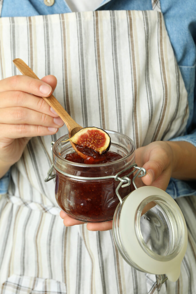 Persoana care baga o lingura de lemn intr-un borcan cu dulceata de smochine. Imagine de aproape