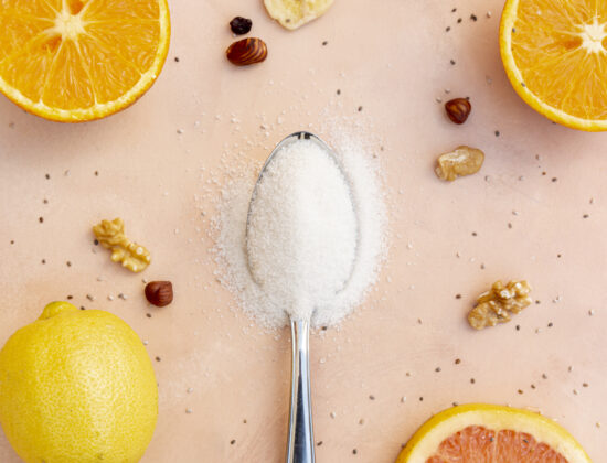 Lingura de fructoza in mijlocul unor citrice, pe fundal colorat