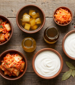 Alimente bogate în probiotice - kombucha, iaurt, tofu - în boluri pe o masă din lemn.