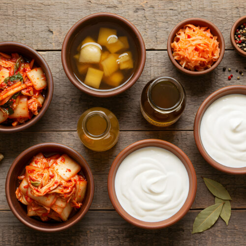 Alimente bogate în probiotice - kombucha, iaurt, tofu - în boluri pe o masă din lemn.