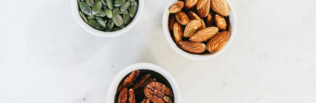 Trei boluri conținând semințe și nuci diverse pe o masă albă - alimentele sunt bogate în Omega-3