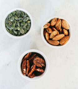 Trei boluri conținând semințe și nuci diverse pe o masă albă - alimentele sunt bogate în Omega-3